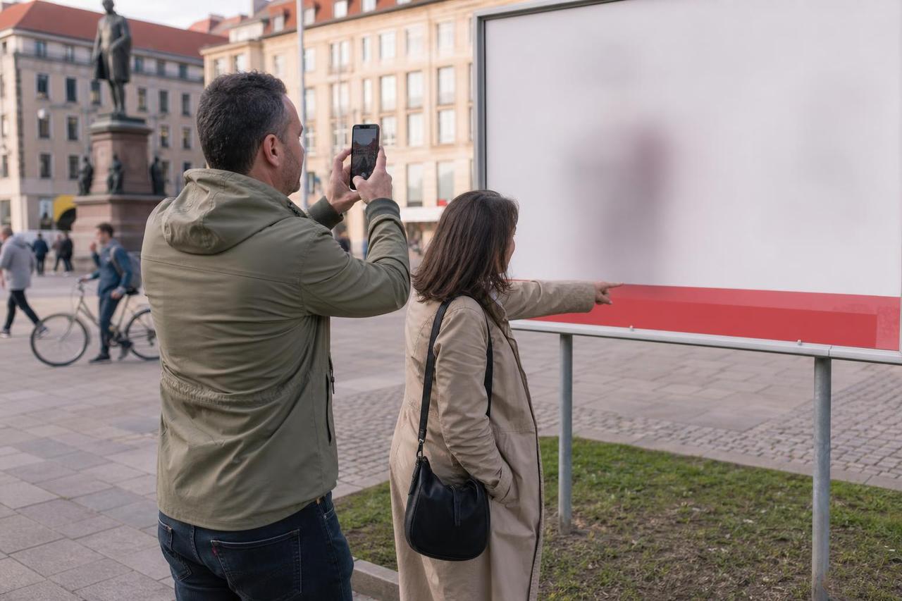 Ein Bürger fotografiert ein politisches Werbeplakat, während seine Begleiterin auf den Hinweisbereich zeigt.