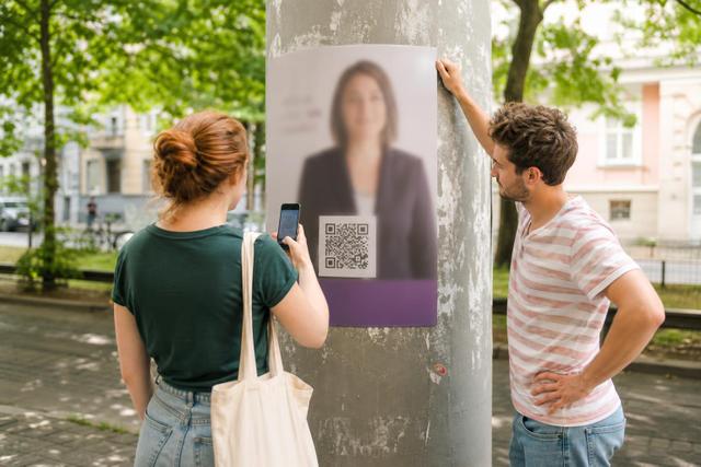 Zwei Ehrenamtliche prüfen den QR-Code eines Wahlplakats mit einem Smartphone.
